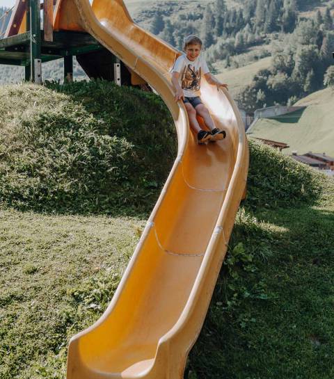 Kind rutscht auf der Outdoor-Rutsche im Abenteuerspielplatz des Familienhotels Oberkarteis