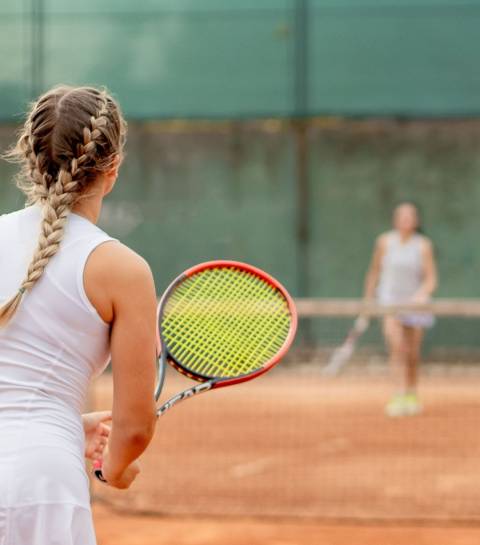 Zwei Frauen spielen Tennis auf einem Tennisplatz, eine Spielerin im Vordergrund mit Tennisschläger – Sportangebot nahe dem Familienhotel Oberkarteis