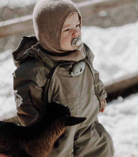 Kleinkind steht draußen mit einer Ziege im Winter im Familienhotel Oberkarteis.