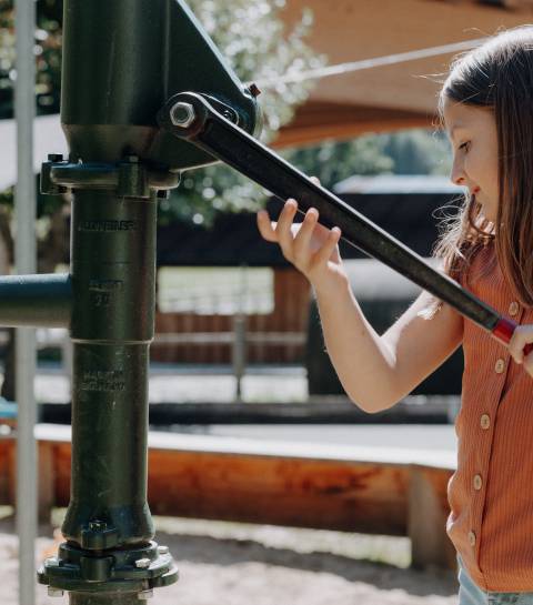 Mädchen bedient die Wasserpumpe im Wasserspielbereich der Outdoor-Spielwelt im Familienhotel Oberkarteis