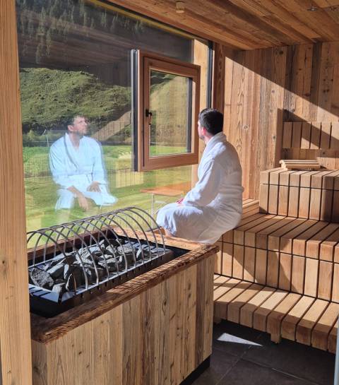 Mann sitzt in Sauna mit großem Fenster und Bergpanorama im Wellnessbereich