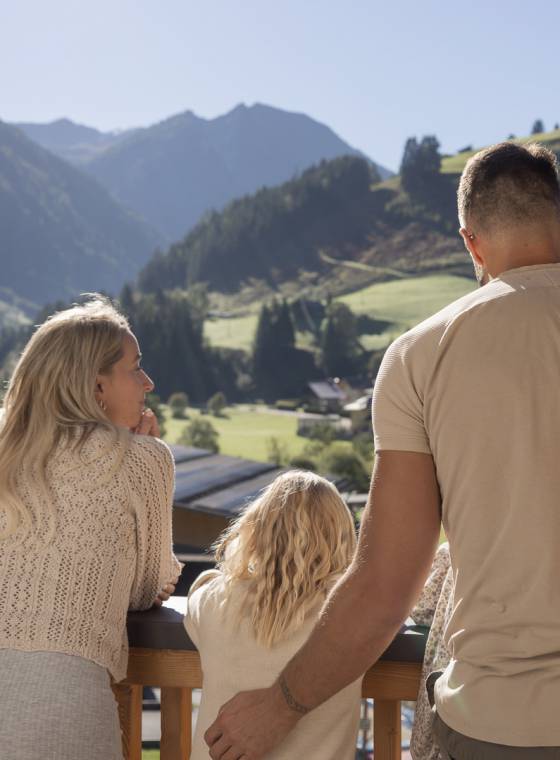 Familie genießt den Ausblick vom Balkon auf die umliegenden Berge im Salzburger Land.