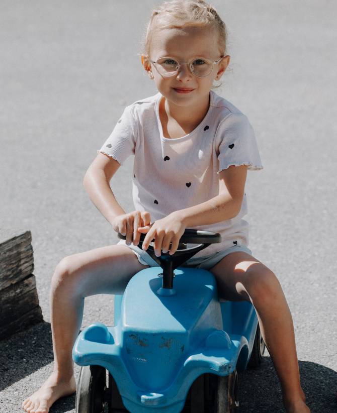 Mädchen fährt barfuß mit blauem Bobbycar auf dem Spielplatz im Familienhotel Oberkarteis