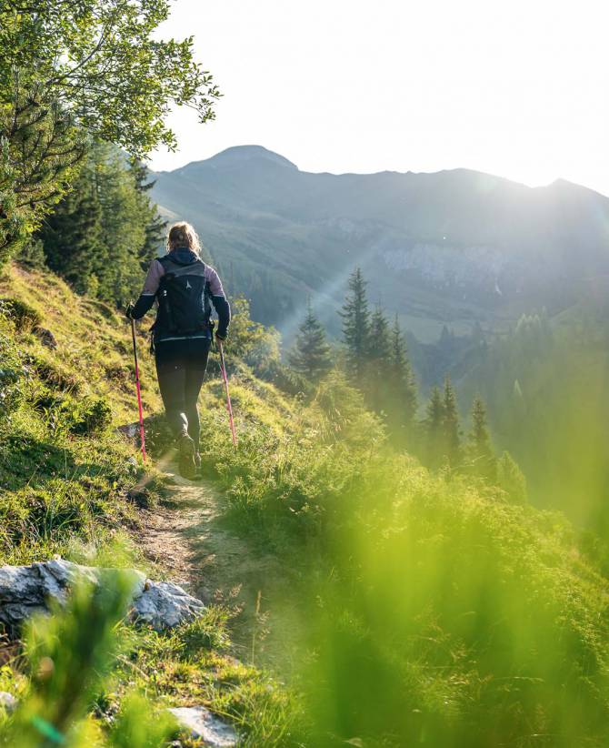 Wanderin mit Stöcken auf einem sonnigen Bergpfad in den Alpen nahe dem Familienhotel Oberkarteis