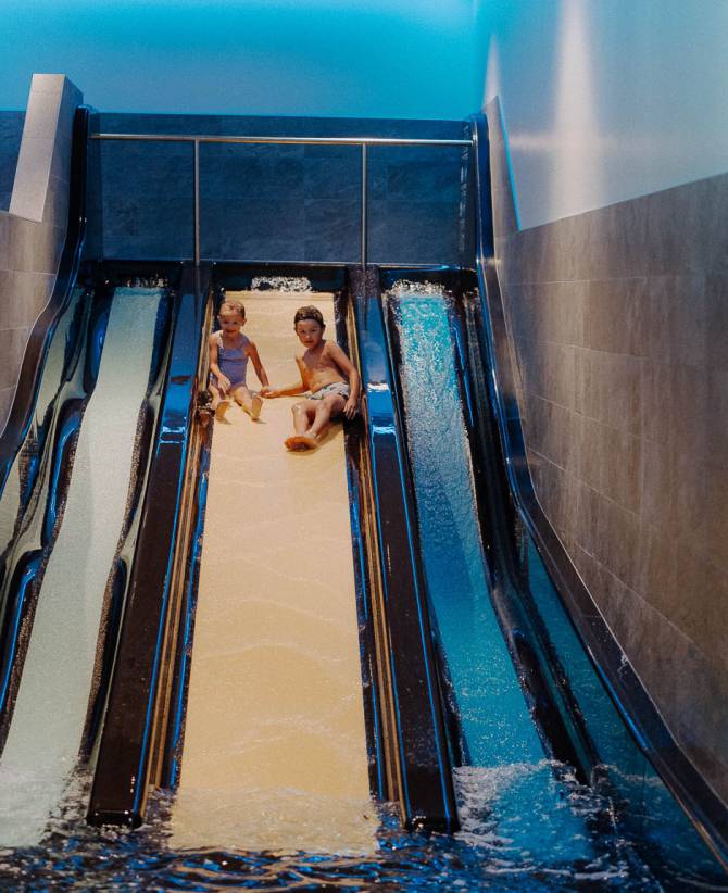 Kinder sausen nebeneinander die breite Wasserrutsche im Hallenbad im Großarltal hinunter