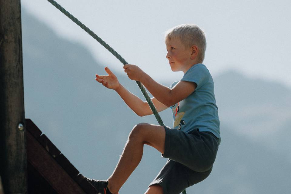Junge klettert am Seil auf dem Abenteuerspielplatz im Salzburger Land nahe dem Familienhotel Oberkarteis