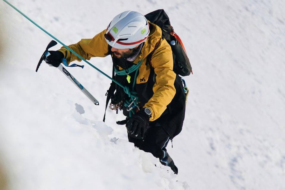 Bergsteiger mit Helm und Eispickel steigt gesichert eine steile Schneefläche hinauf im Salzburger Land