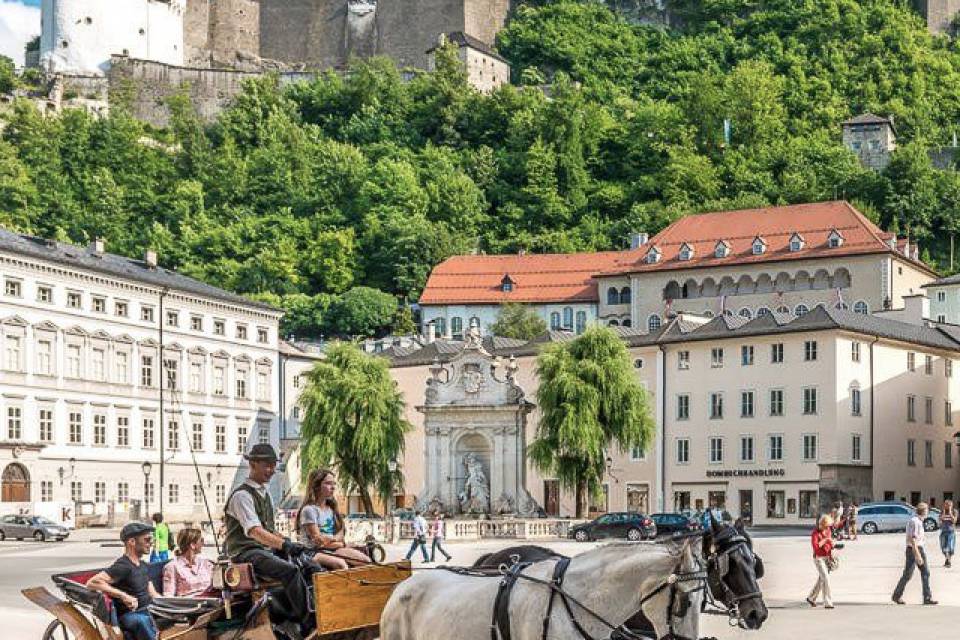 Pferdekutsche auf einem Platz in Salzburg mit Festung Hohensalzburg im Hintergrund – Städtausflug vom Familienhotel Oberkartei