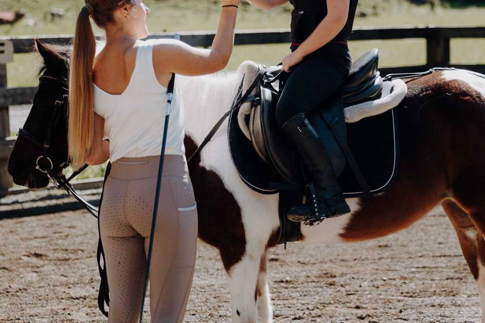 Kind auf Pony gibt Reitlehrerin High Five nach erfolgreicher Reitstunde im Familienhotel Oberkarteis