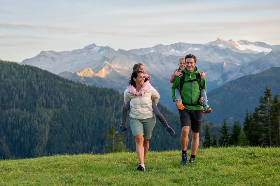 Familie mit Kindern huckepack auf Almwiese mit Alpenpanorama im Großarltal