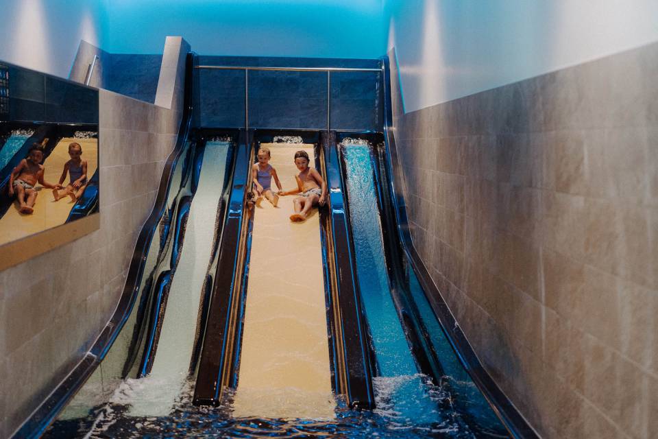 Kinder sausen nebeneinander die breite Wasserrutsche im Hallenbad im Großarltal hinunter