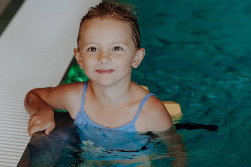 Mädchen schwimmt im Hallenbad am Beckenrand des Familienhotel Oberkarteis