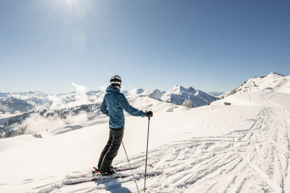 Sportlicher Skifahrer auf breiter, sonniger Skipiste im Winterurlaub in Österreich