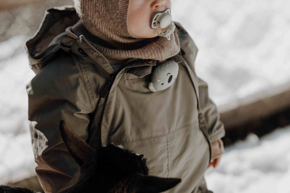 Kleinkind steht draußen mit einer Ziege im Winter im Familienhotel Oberkarteis.