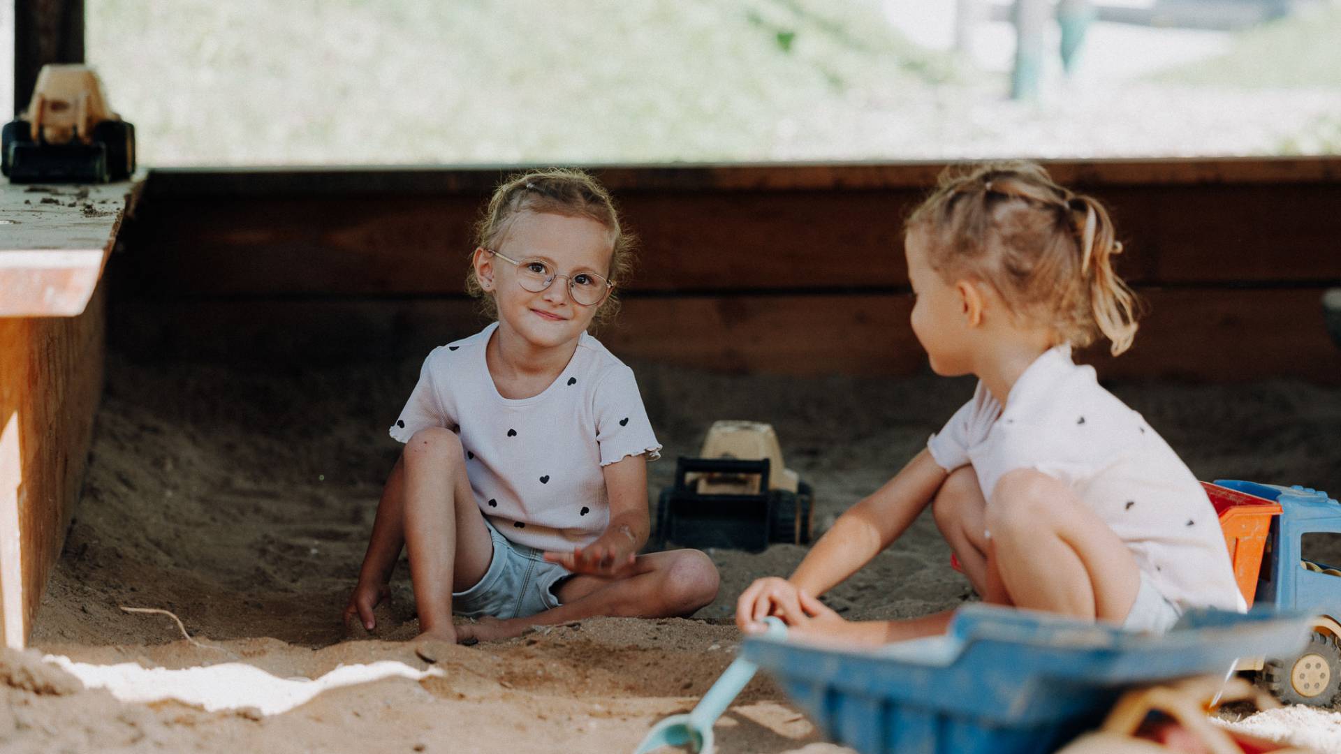 Mädchen spielen gemeinsam im Sandkasten mit Spielzeugfahrzeugen im Familienhotel Oberkarteis