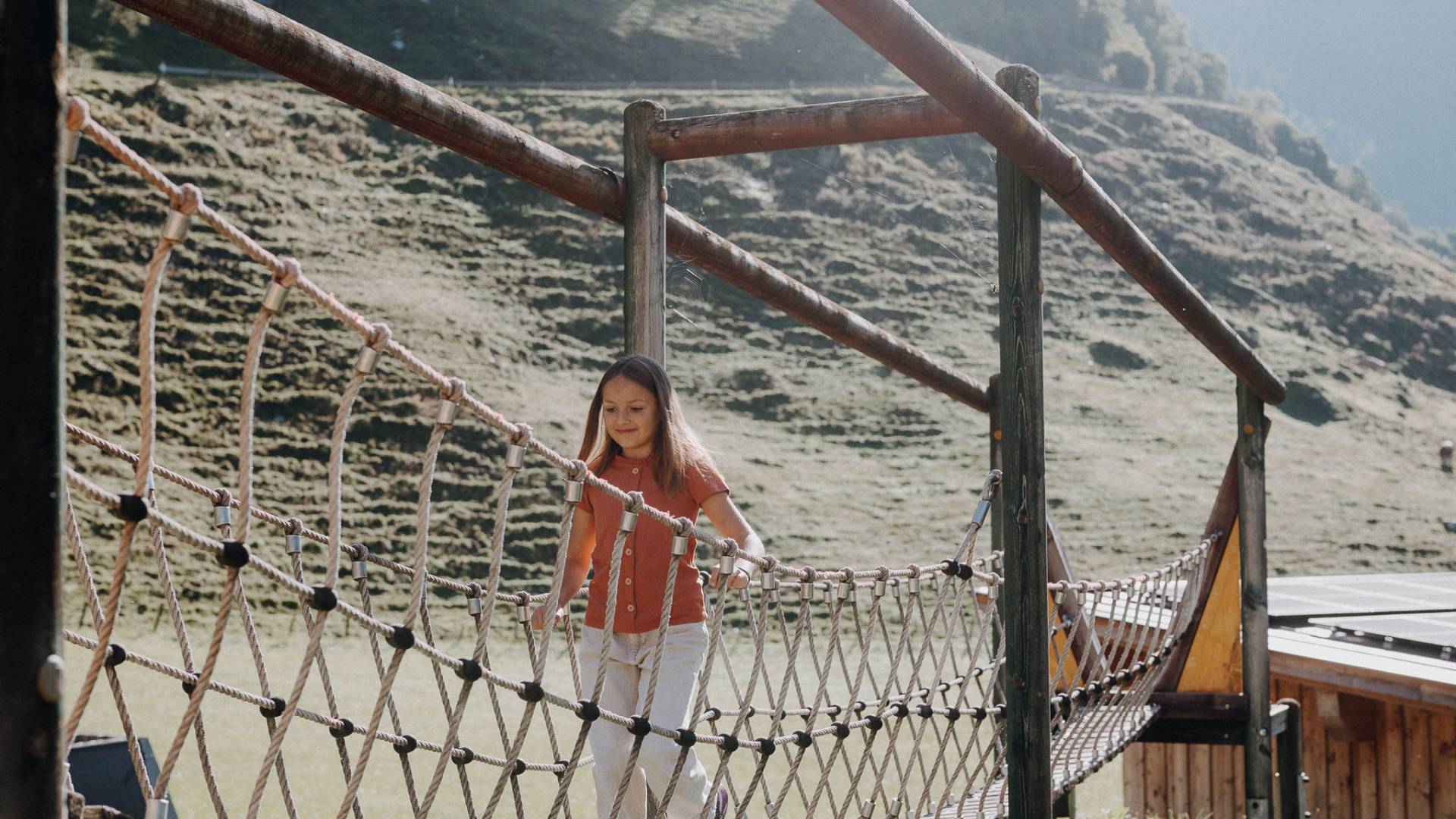 Mädchen klettert im Outdoor-Spielbereich am Kletternetz des Familienhotels Oberkarteis