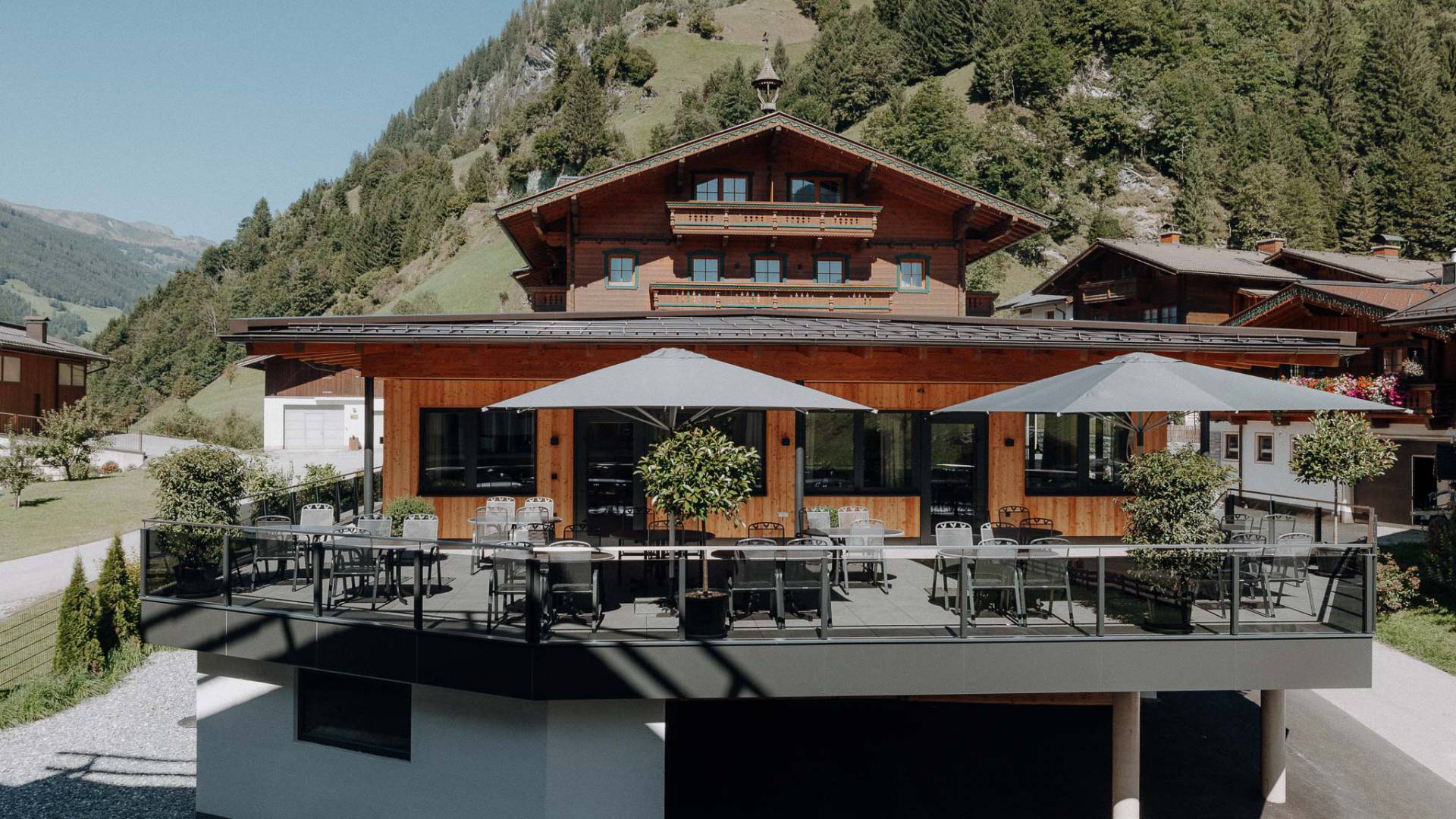 Modern renovierte Sonnenterrasse des Familienhotel Oberkarteis mit Sitzplätzen und Sonnenschirmen vor alpiner Bergkulisse