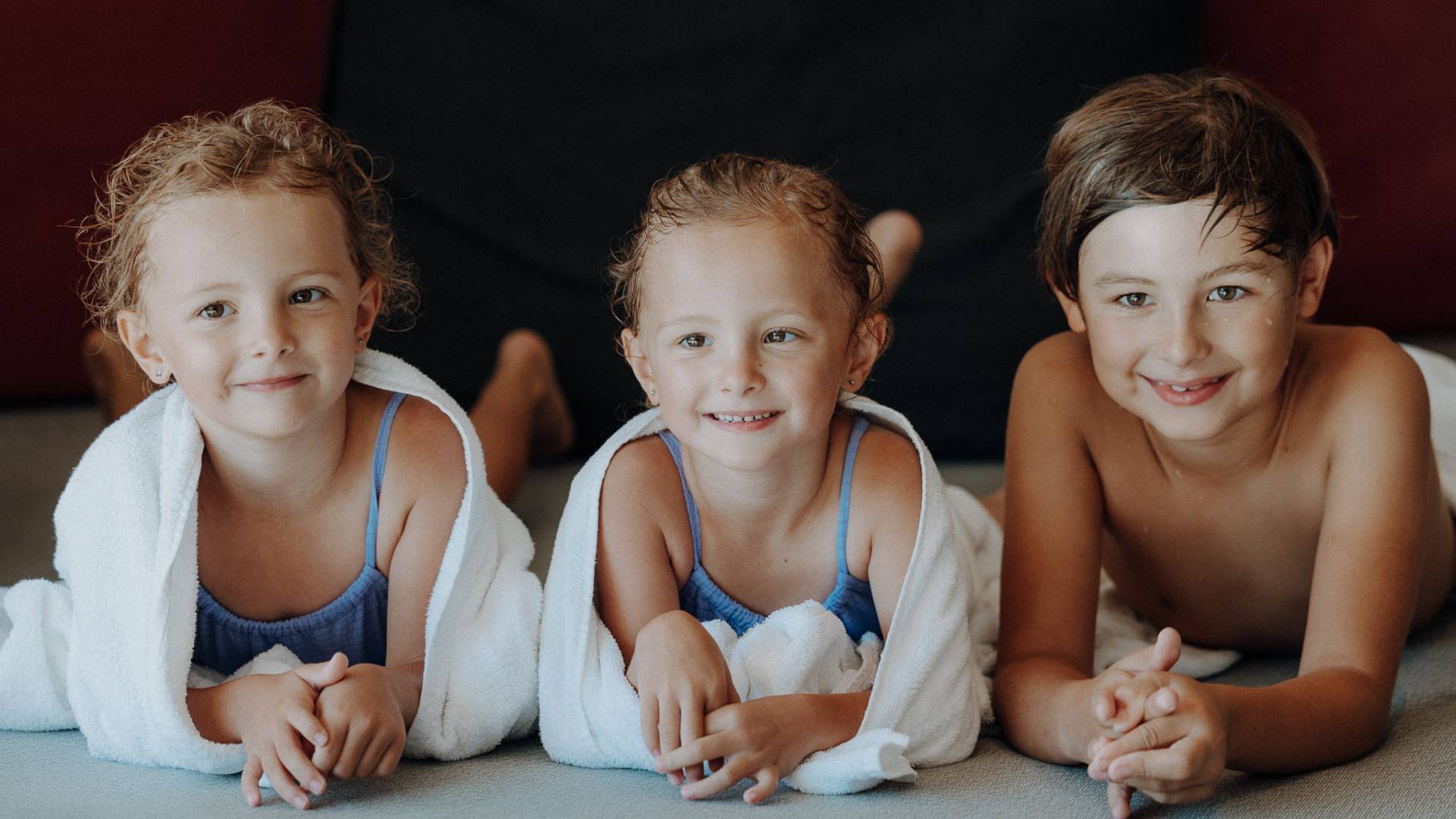 Drei Kinder entspannt auf  dem Bauch liegend auf einer Liege im Poolbereich im Familienhotel Oberkarteis