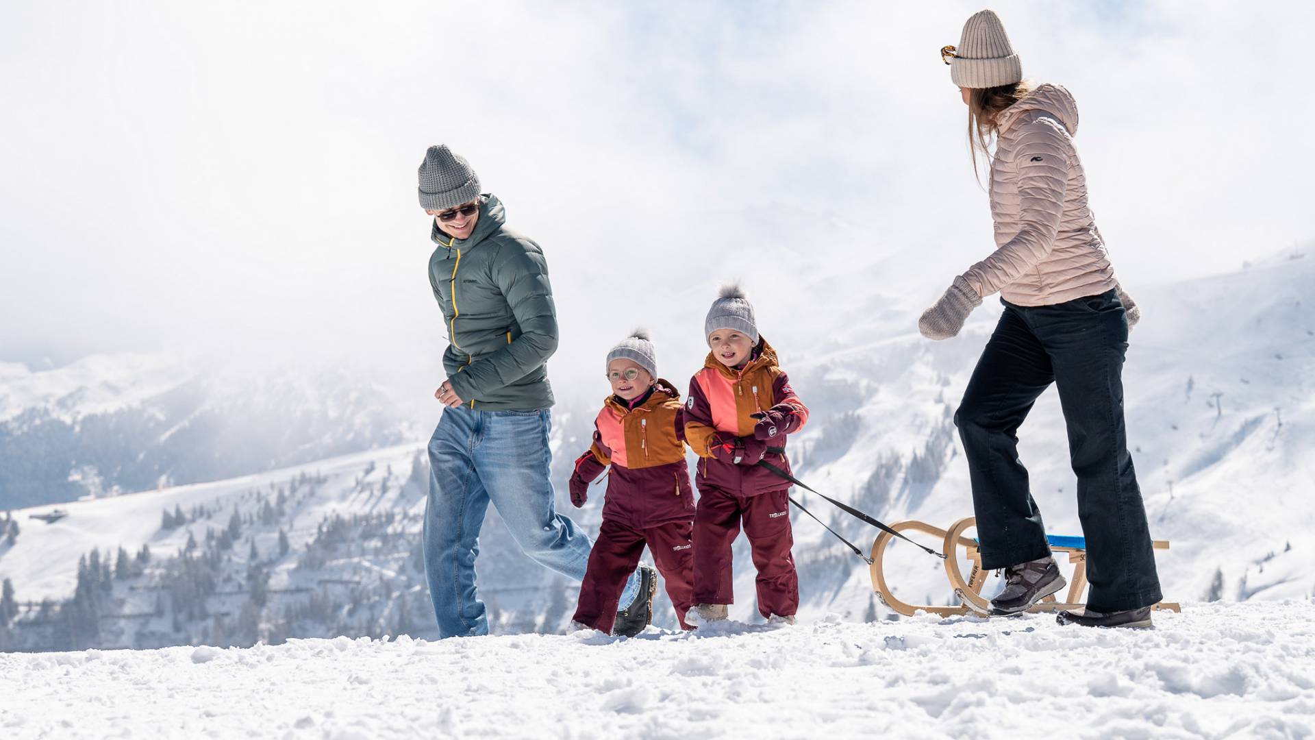 Eltern und Kinder laufen mit Holzschlitten durch die winterliche Alpenlandschaft