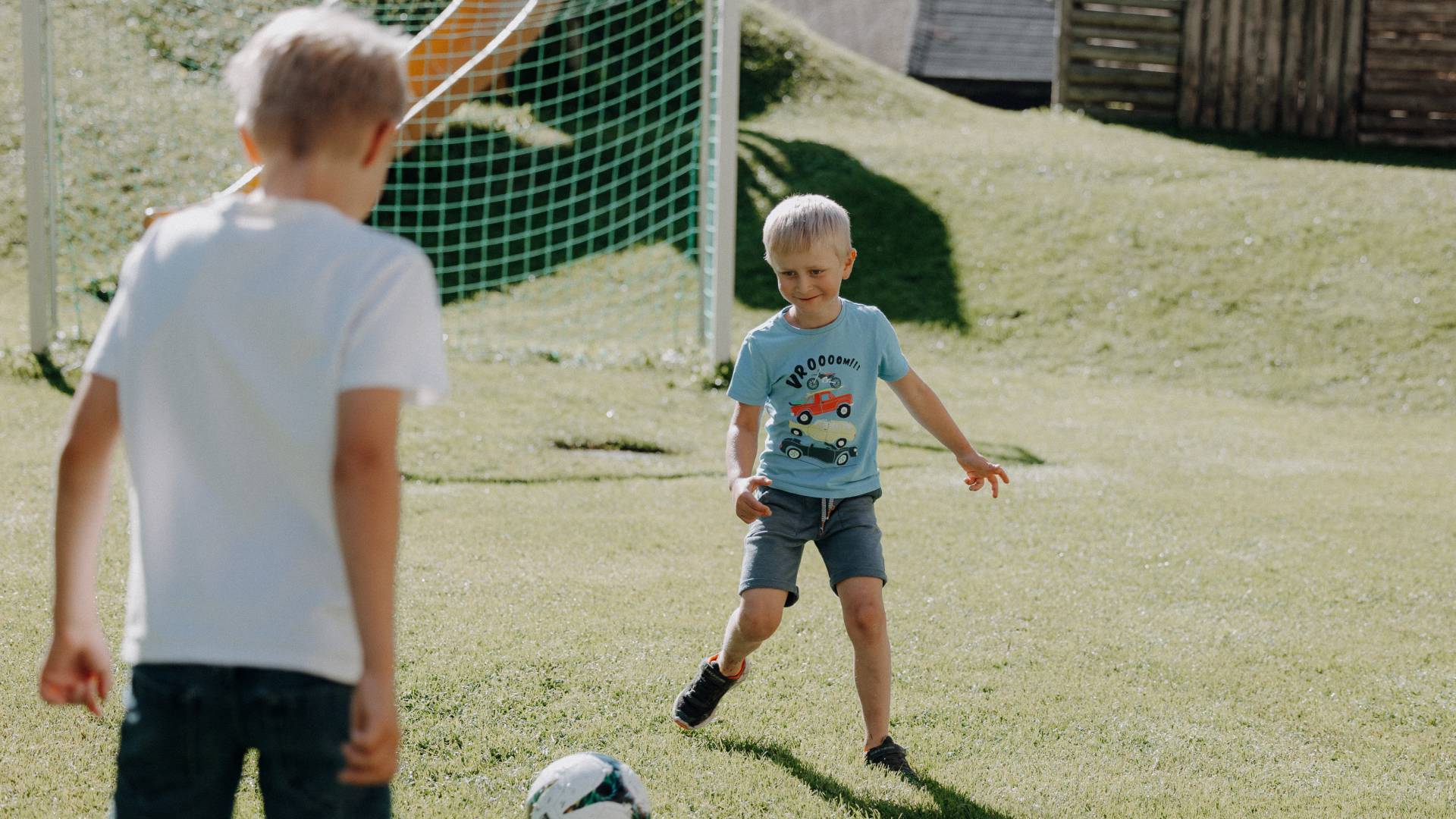 Junge spielt Fußball auf der grünen Wiese mit Blick auf die Berge im Großarltal