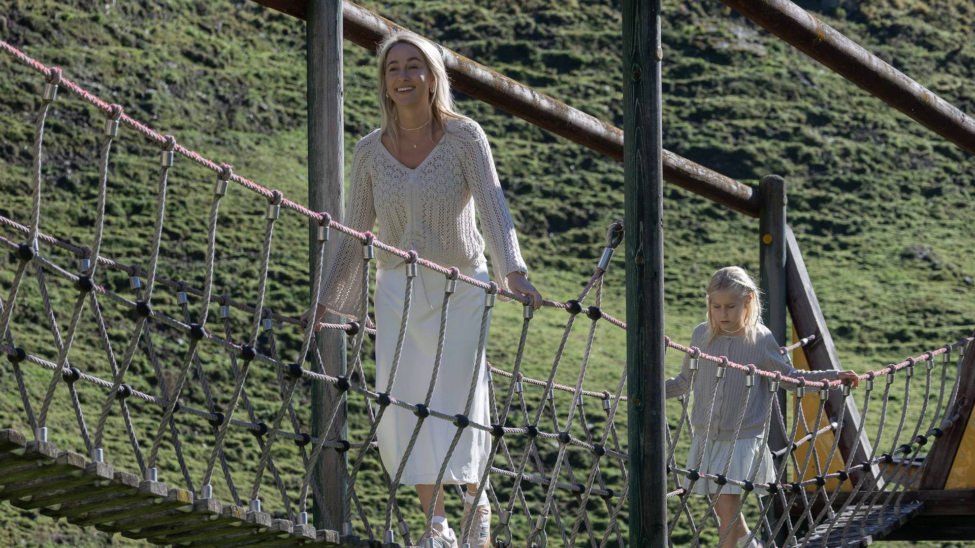 Mama mit Kind auf der Hängebrück des Abenteurspielplatz draußen.
